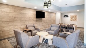 A modern lounge area with grey upholstered chairs, a round table, and a flat-screen TV mounted on the wall.