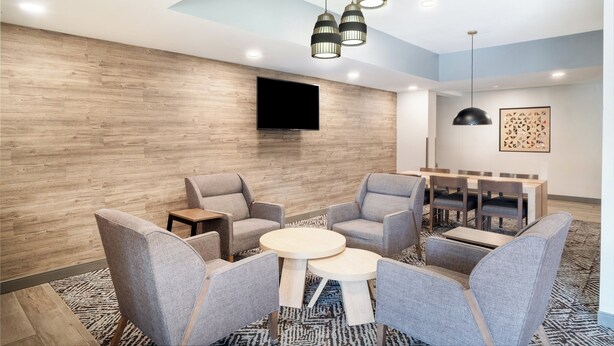 A modern lounge area with grey upholstered chairs, a round table, and a flat-screen TV mounted on the wall. - Candlewood Suites El Paso by IHG (El Paso)