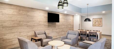 Un espace détente moderne avec des fauteuils gris à revêtement, une table ronde et un téléviseur à écran plat fixé au mur.