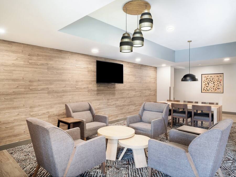 A modern lounge area with grey upholstered chairs, a round table, and a flat-screen TV mounted on the wall.