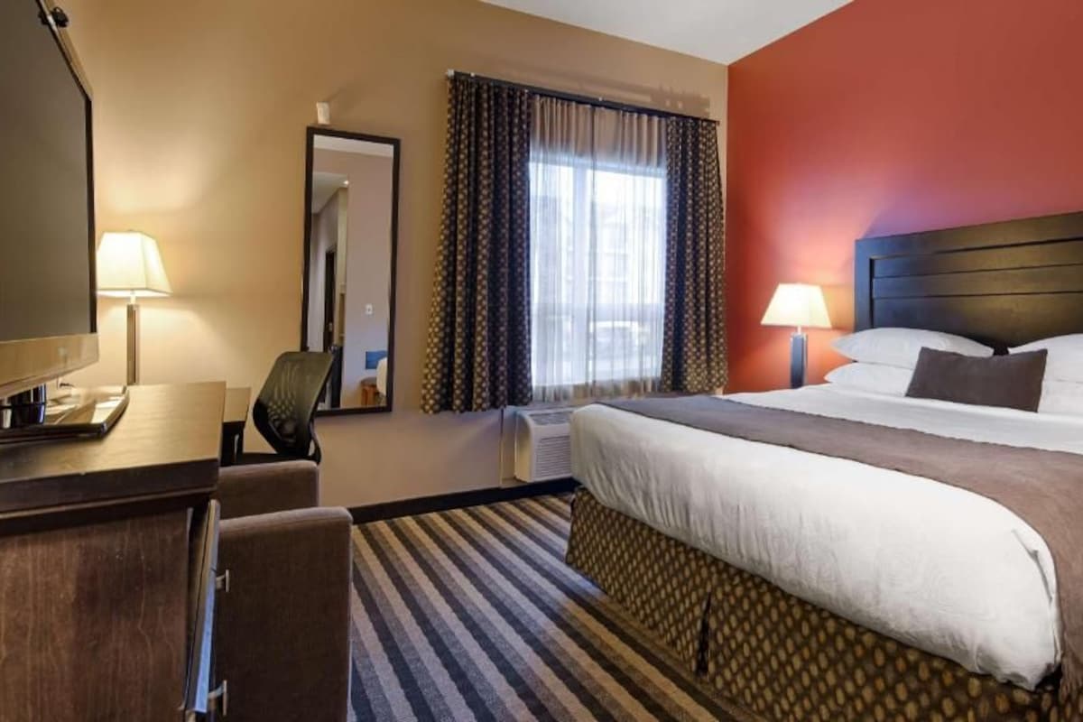 A hotel room with a bed, bedside table, lamp, chair, and a large mirror.