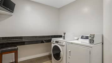 Un cuarto de lavandería con lavadora, secadora y un taburete pequeño.