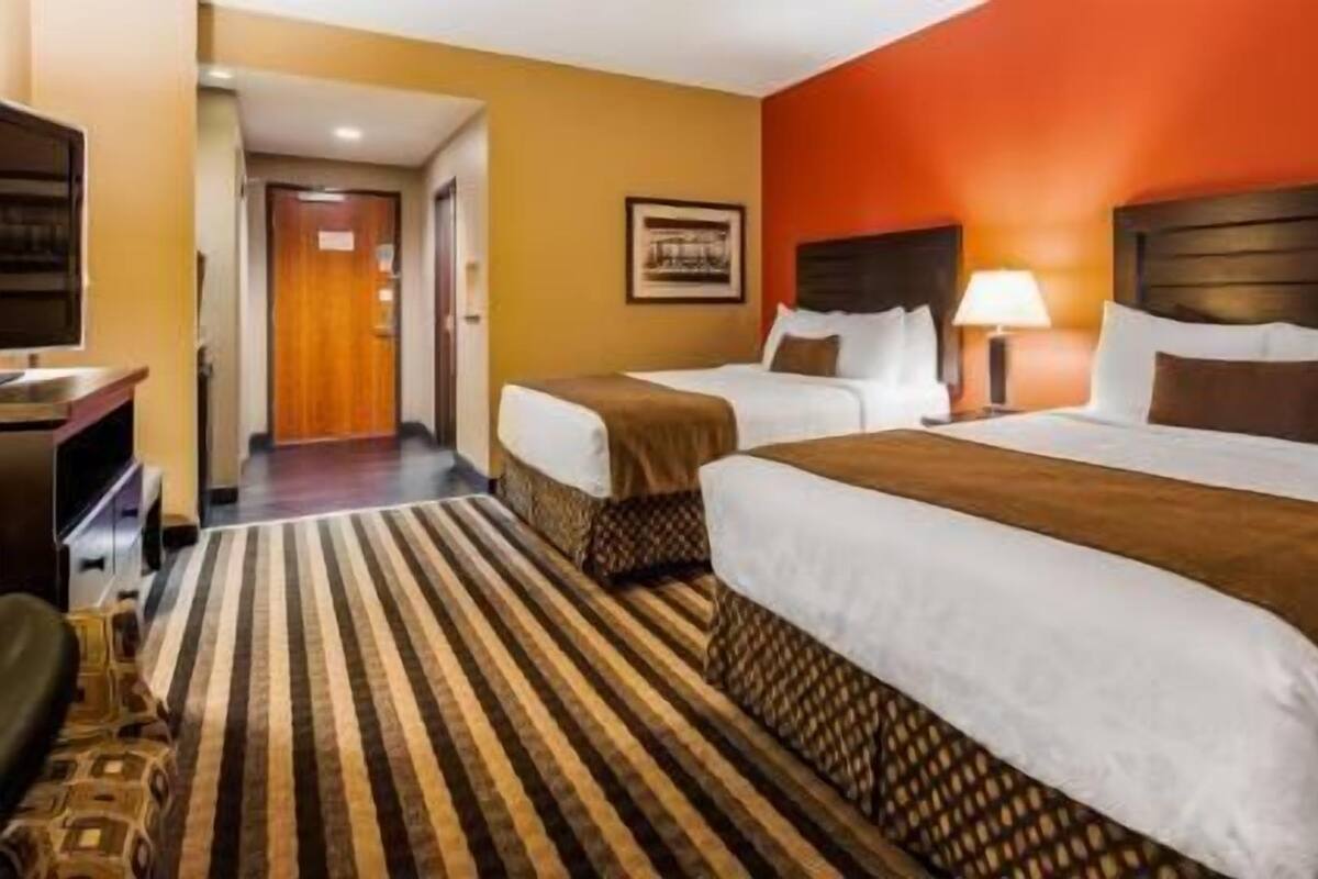 A hotel room with two beds, a striped rug, a wooden headboard, and a desk with a lamp.