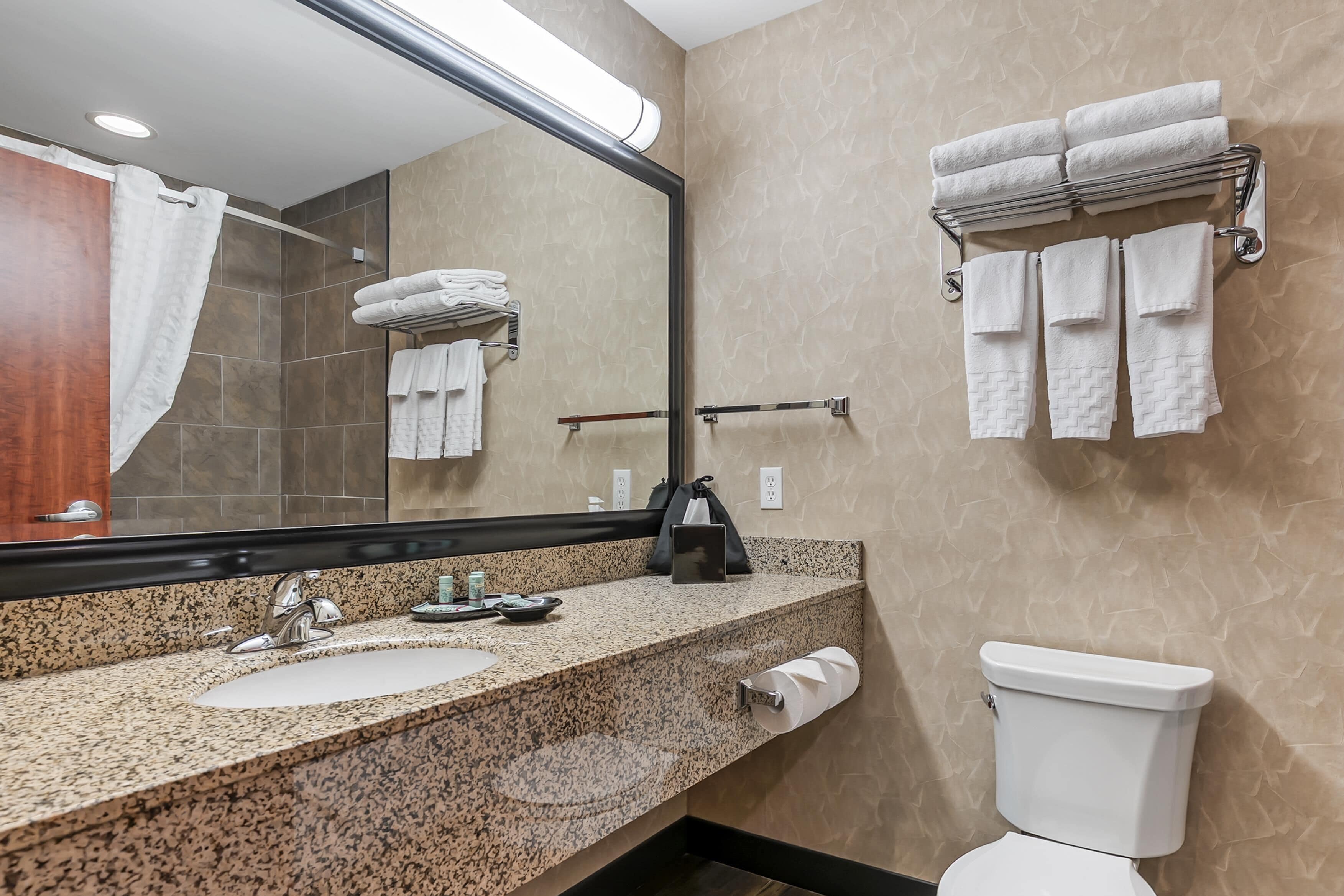 A modern bathroom with a granite countertop, a sink, a mirror, a towel rack, and a toilet.