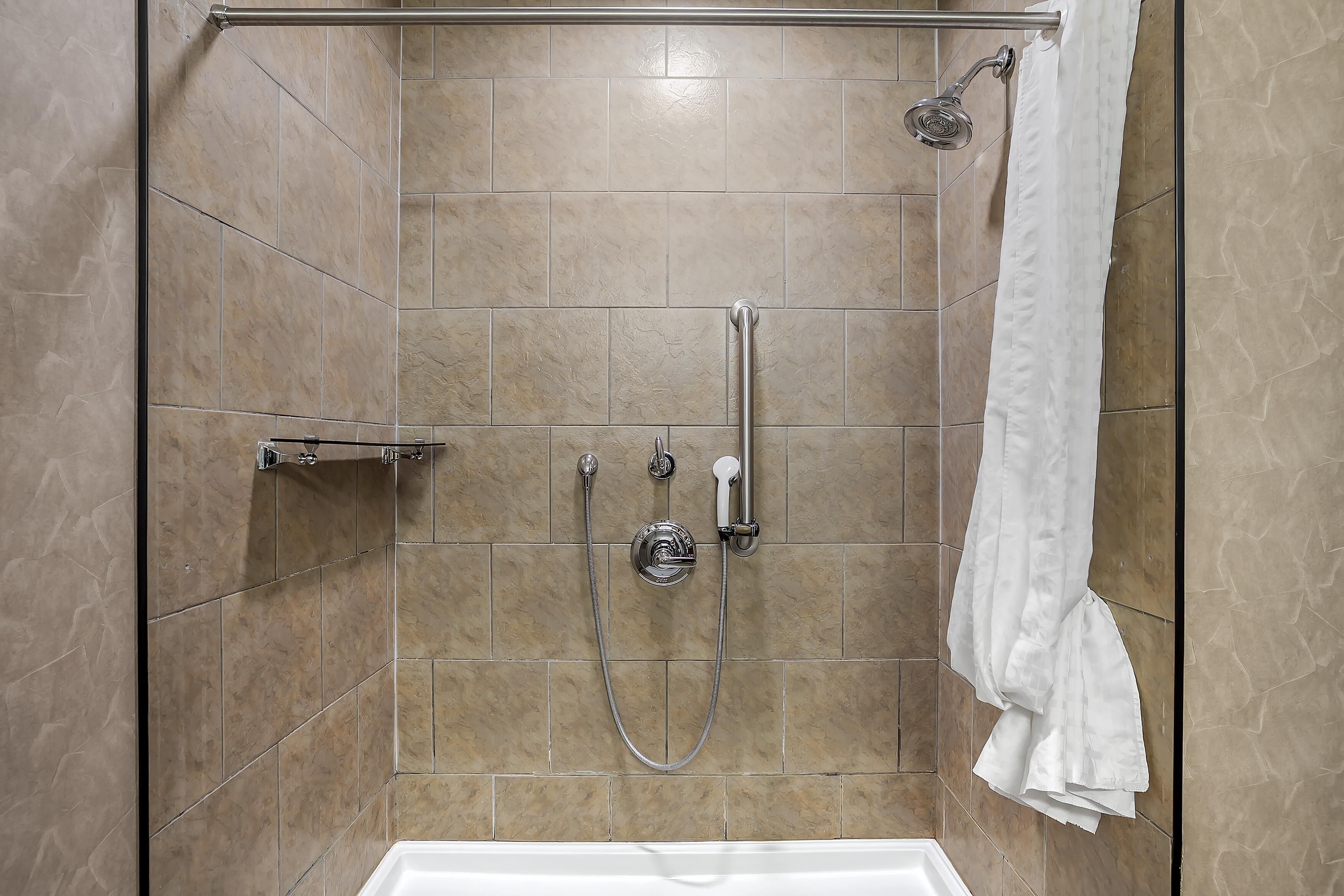 Zona de ducha con mampara de vidrio, ducha de mano, grifo empotrado en la pared y una toalla blanca colgada.