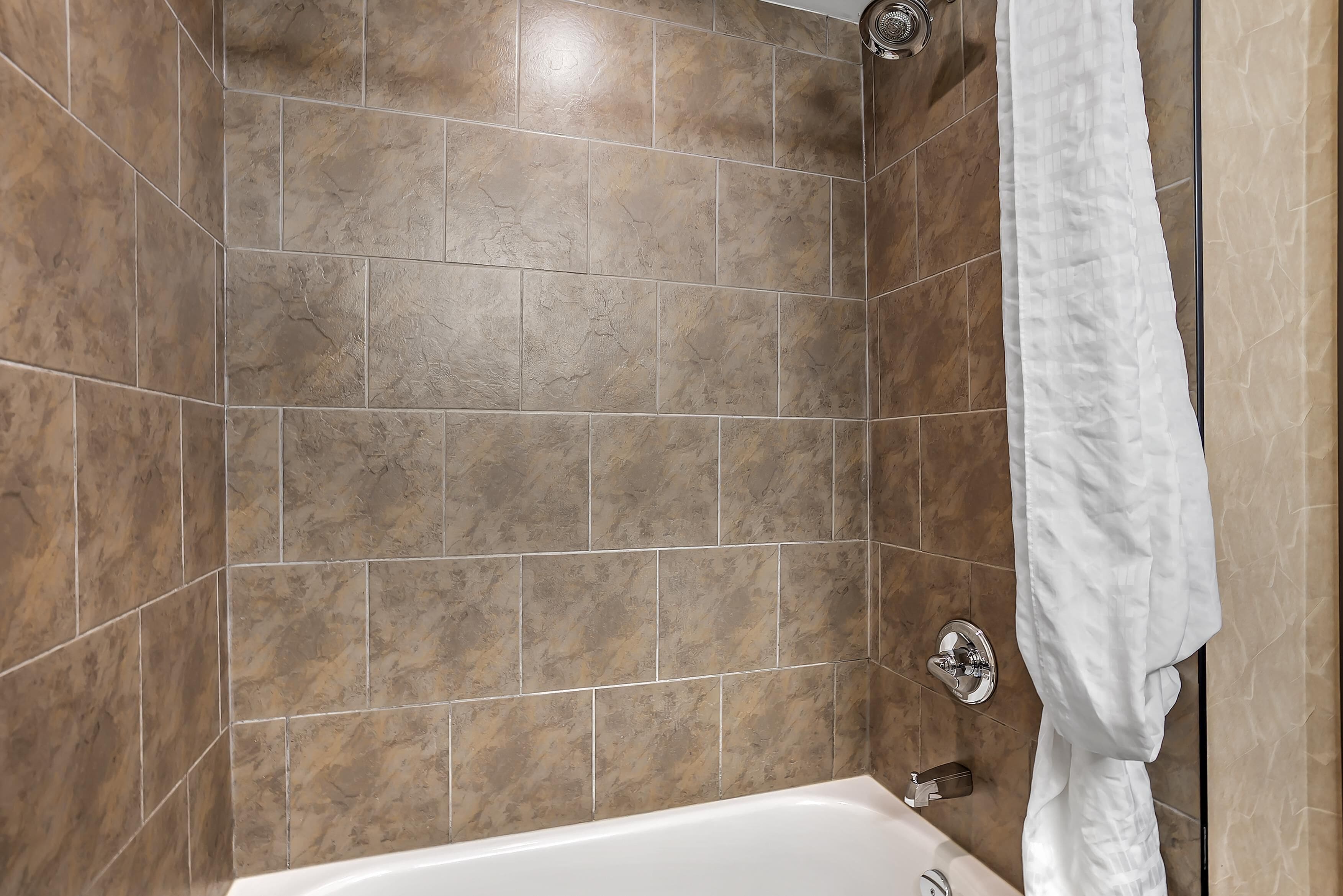Ein Badezimmer mit braunen Fliesen, einer weißen Badewanne und einem weißen Handtuch an der Wand.