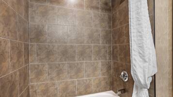 Ein Badezimmer mit braunen Fliesen, einer weißen Badewanne und einem weißen Handtuch an der Wand.