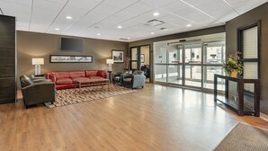 Eine geräumige Lobby mit einer roten Ledersofa, Holzboden und einem großen Fenster mit Blick nach außen.