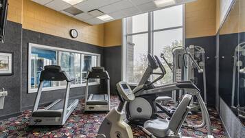 Un gimnasio con cintas de correr, elíptica y máquina de pesas.