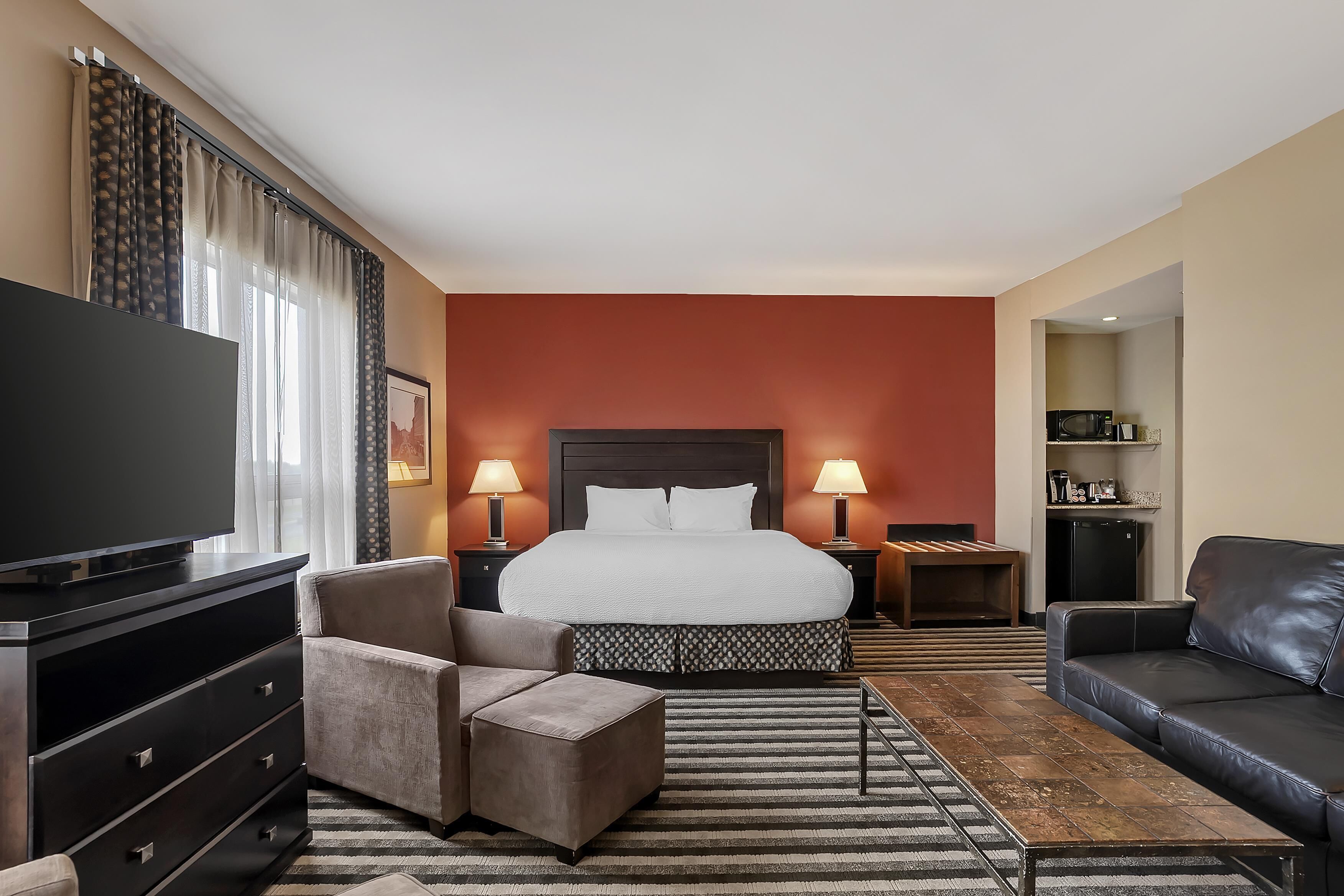 A hotel room with a large bed, a TV, a sofa, a desk, and a dresser.