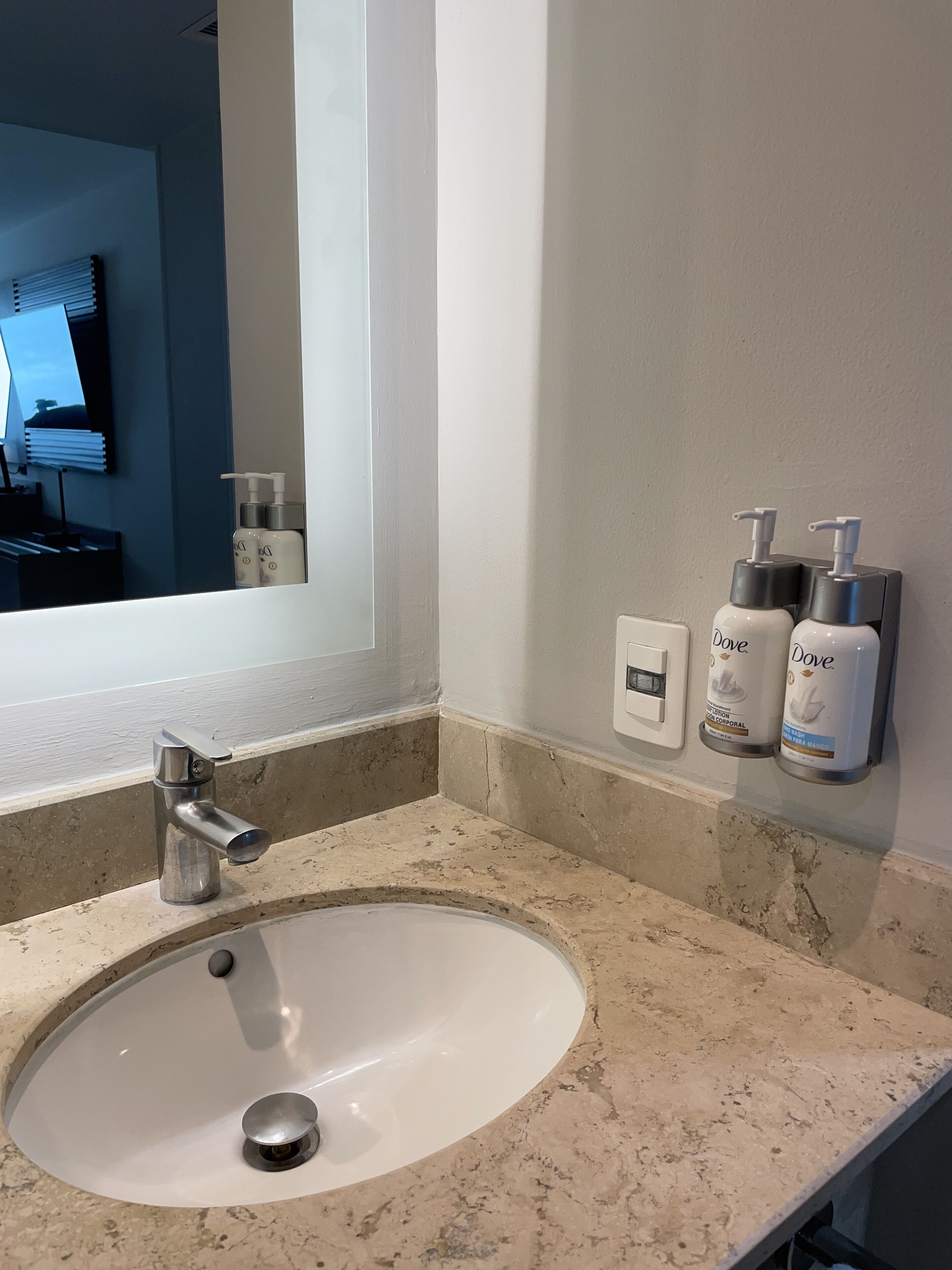 A bathroom with a white sink, a mirror, and two Dove lotion dispensers on the wall.