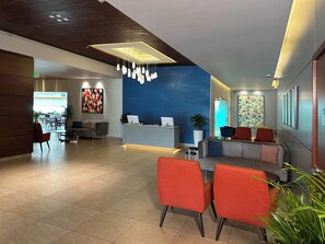 A modern hotel lobby with a reception desk, seating area, and a large blue patterned wall.