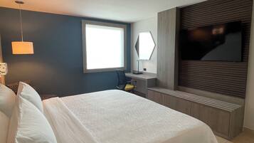Habitación de hotel moderna con una cama grande, un escritorio, una silla, un televisor de pantalla plana y una ventana que proporciona luz natural.