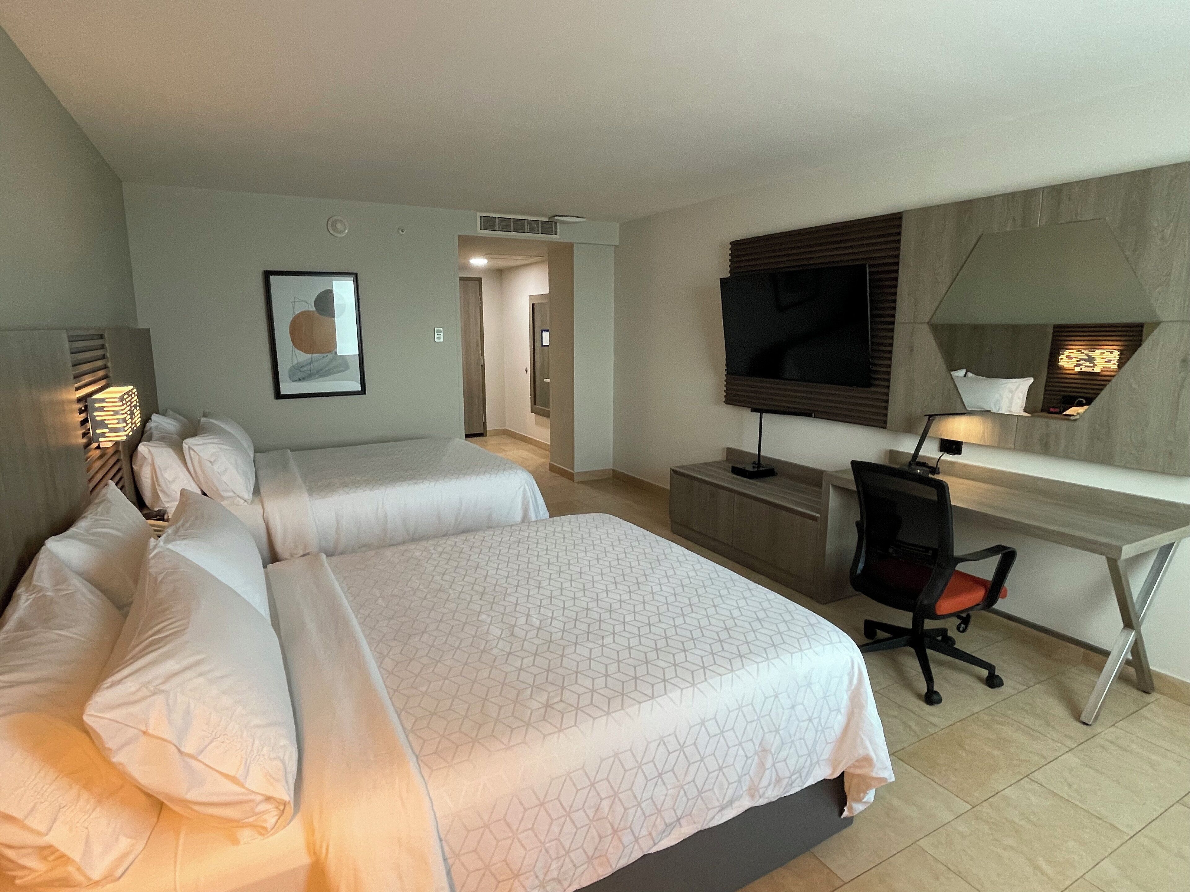 A hotel room with two beds, a desk, a chair, a TV, and a framed picture on the wall.