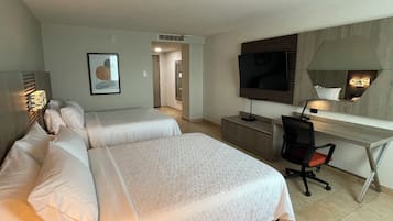 A hotel room with two beds, a desk, a chair, a TV, and a framed picture on the wall.