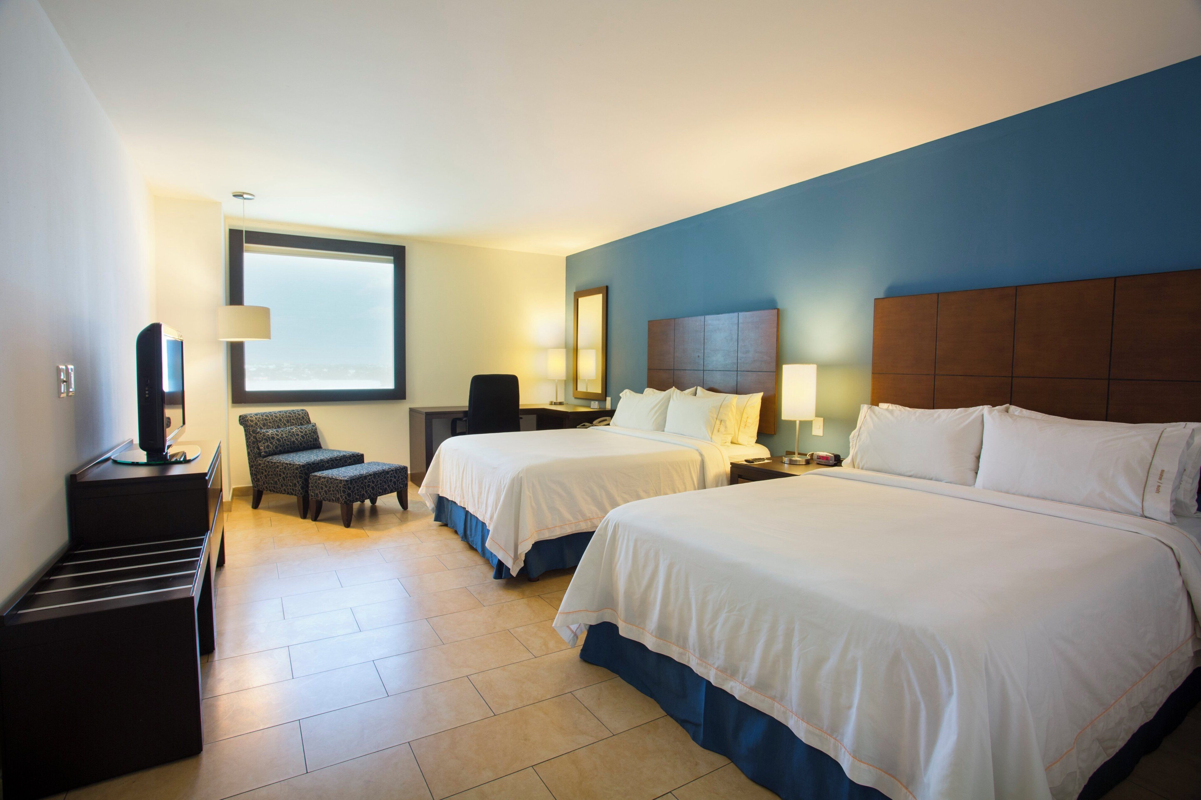 A hotel room with two beds, a desk, a chair, and a television.