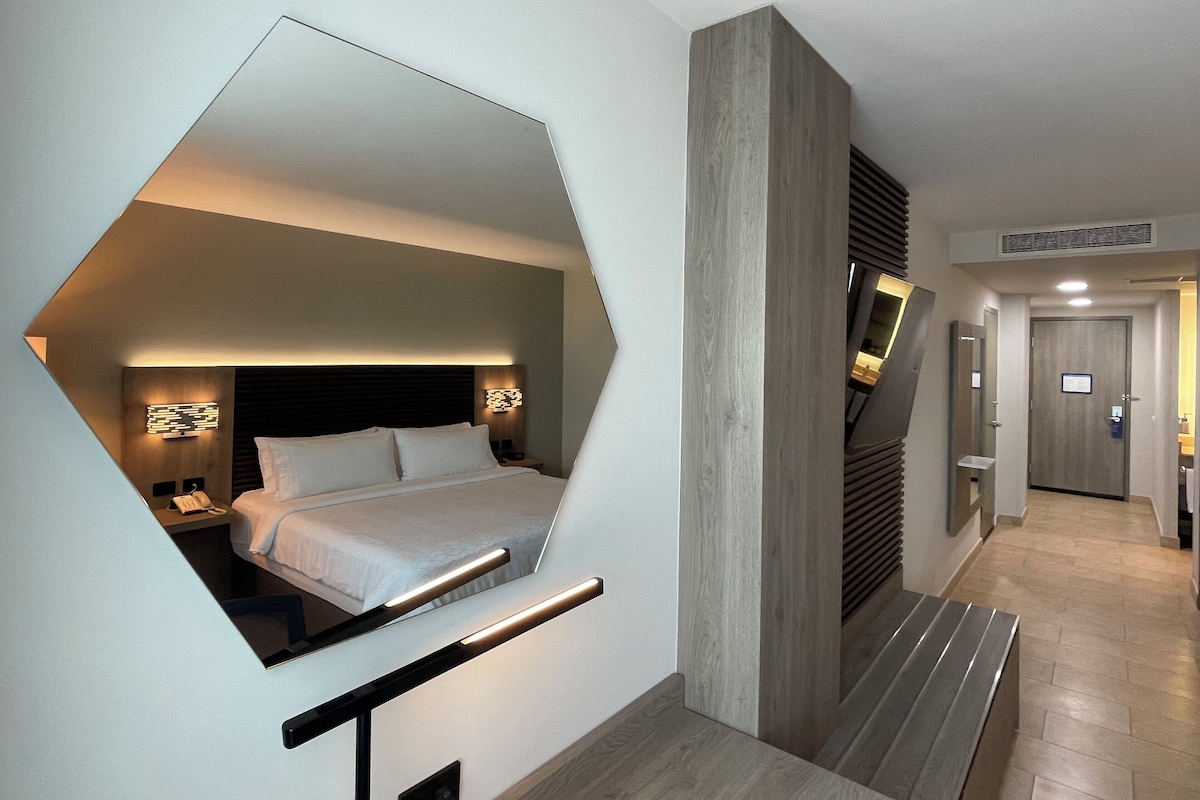 Quarto de hotel moderno com design geométrico marcante, uma cama grande e área de trabalho integrada.