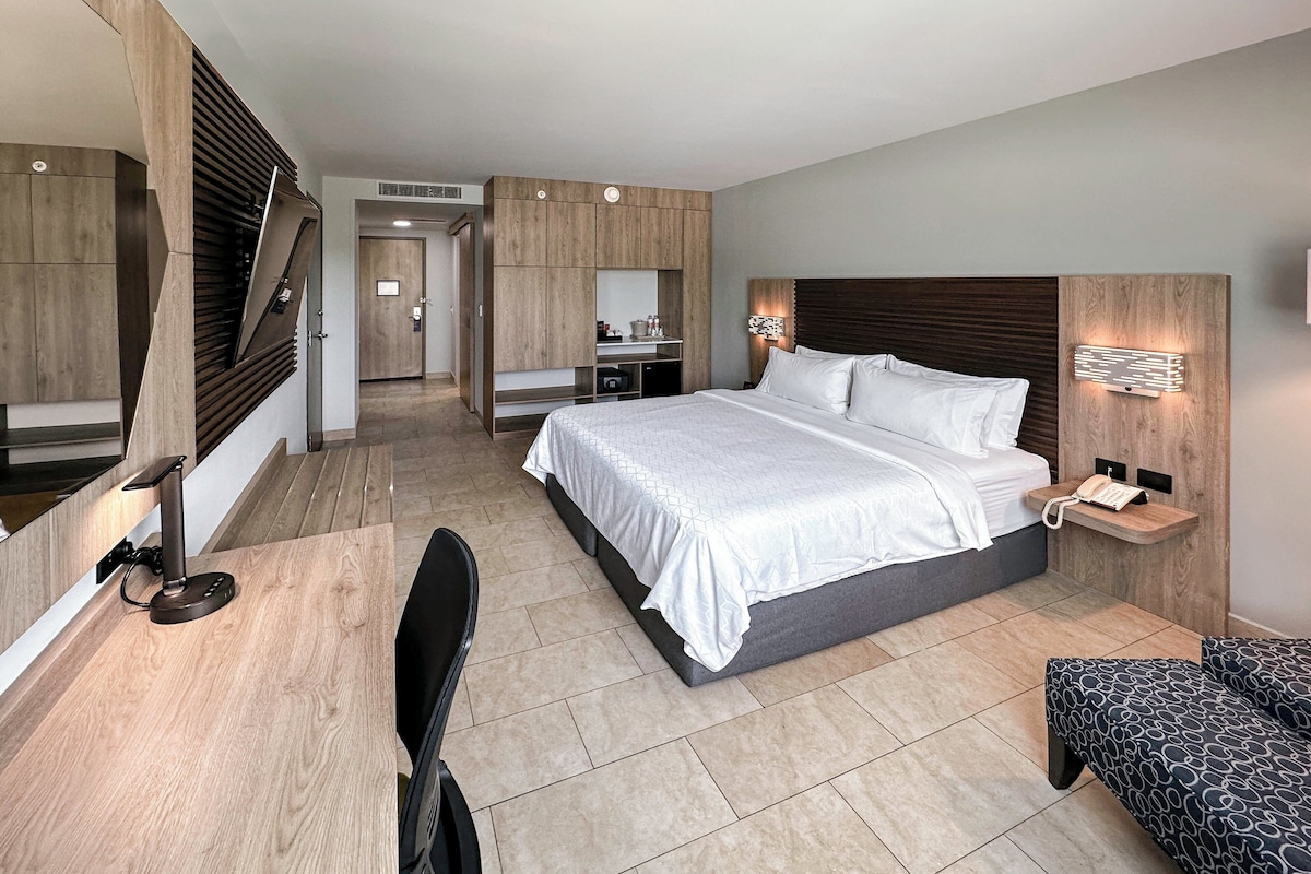 Quarto de hotel moderno com uma cama grande, uma escrivaninha, uma cadeira e um pequeno espaço de estar.