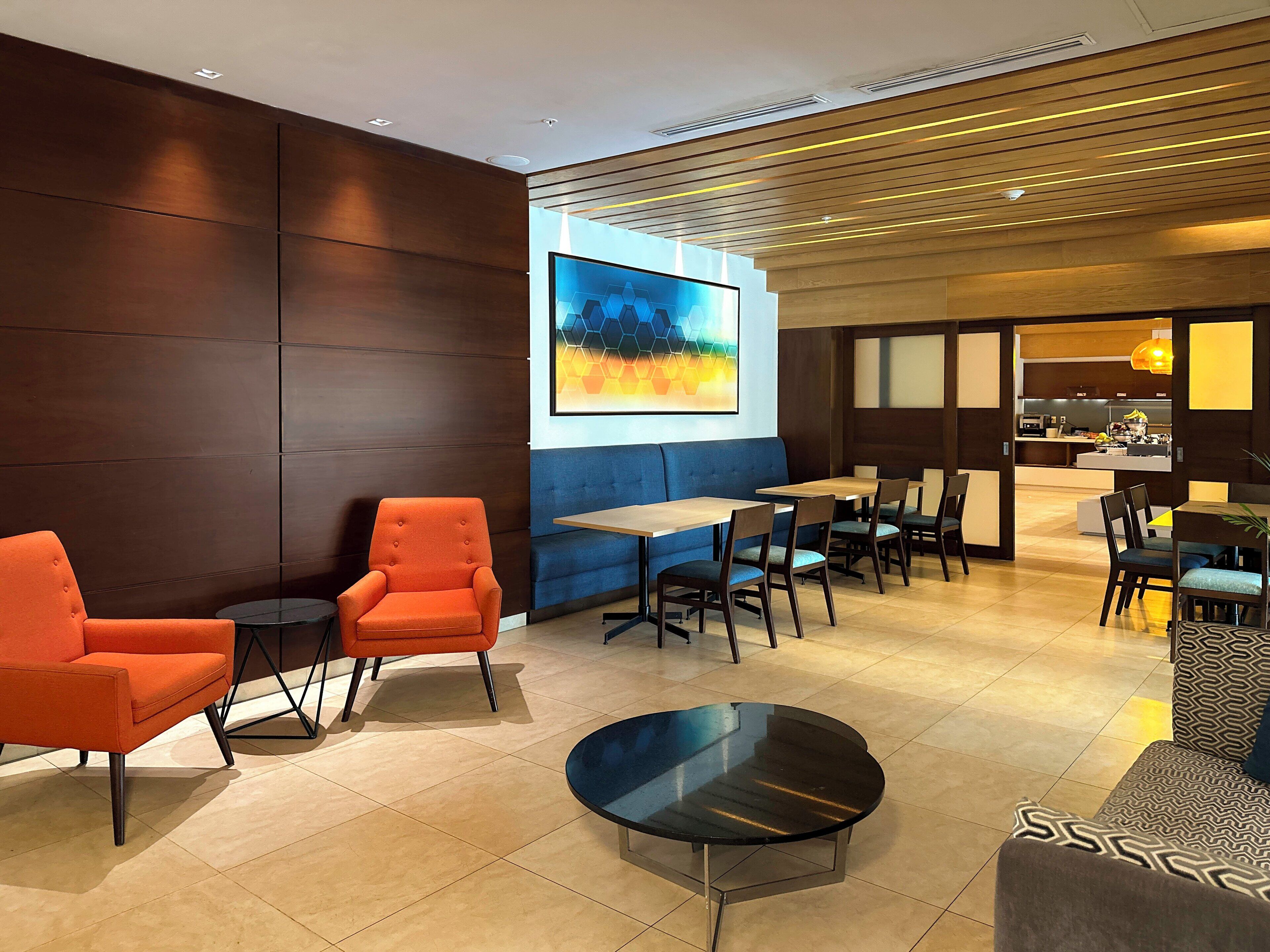 A modern lounge area with seating, a coffee table, and a large wall-mounted screen.