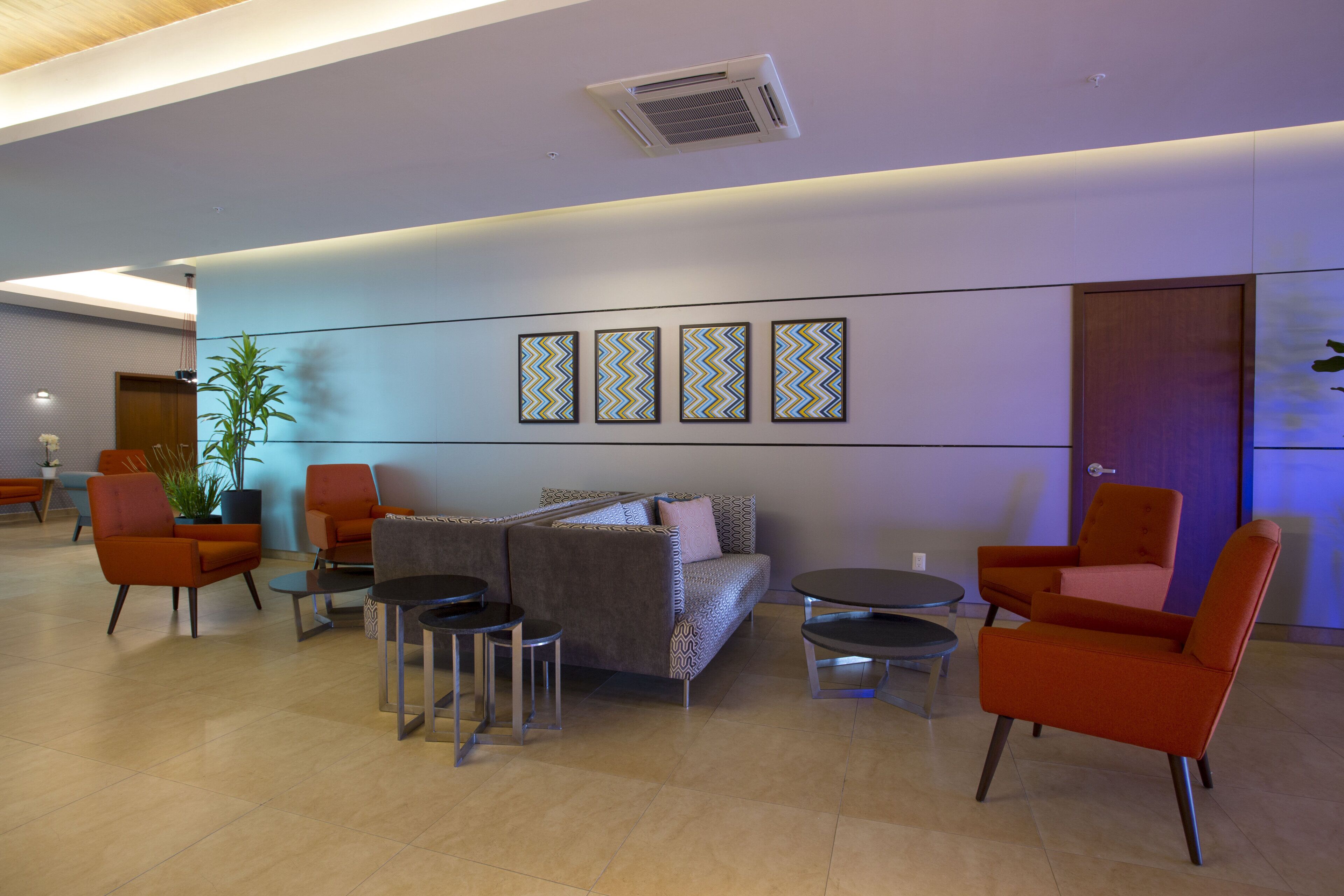A lobby with a sofa, chairs, and a small table. There are wall-mounted artworks and a ceiling vent.