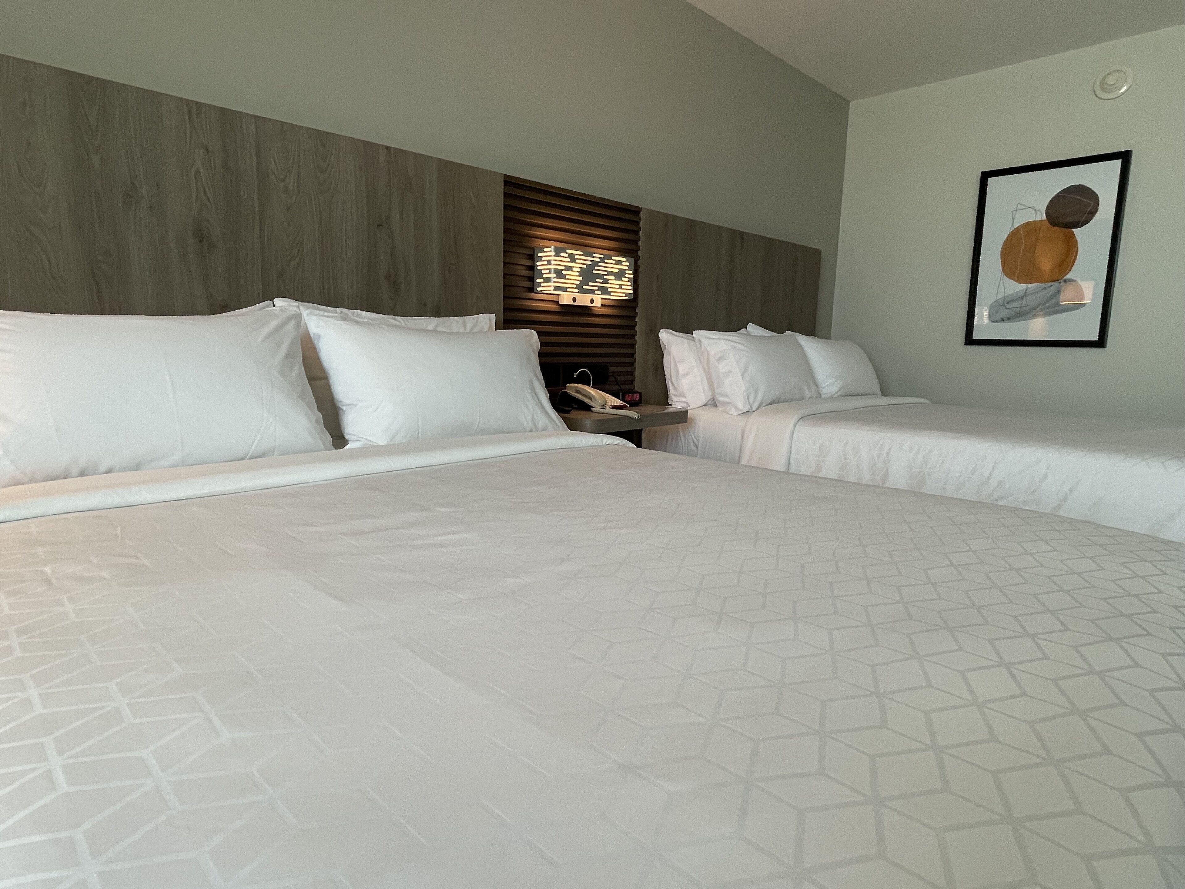A hotel room with two beds, a wooden headboard, a nightstand with a lamp, and a framed picture on the wall.