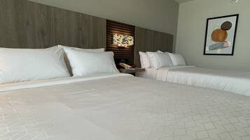 A hotel room with two beds, a wooden headboard, a nightstand with a lamp, and a framed picture on the wall.