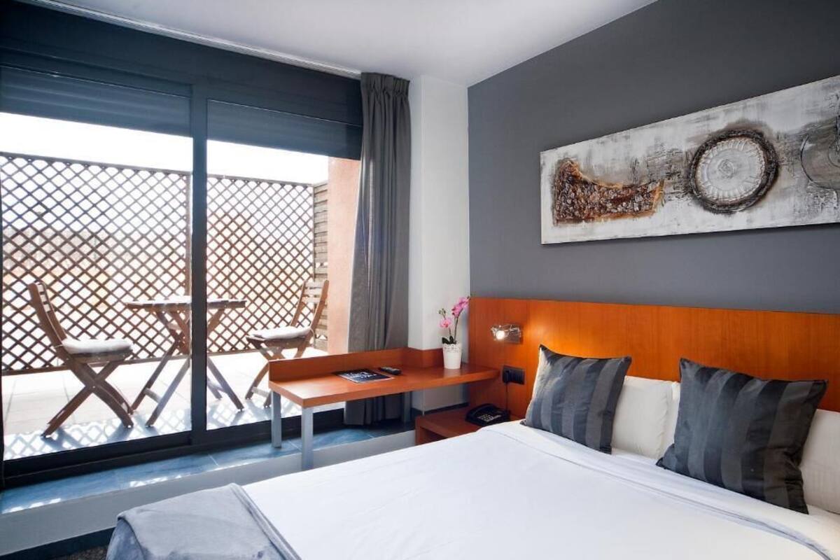 A hotel room with a bed, a desk, a chair, and a large window.
