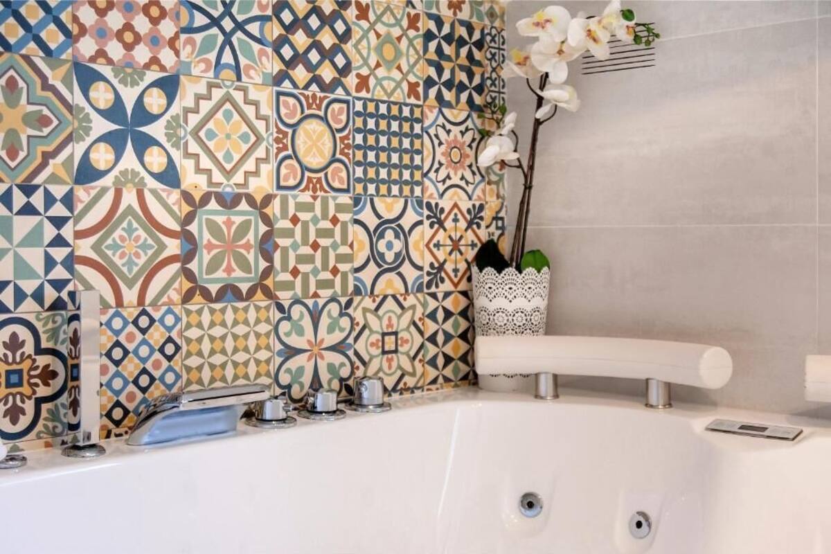 A bathroom with a white bathtub, a sink, and a decorative wall with patterned tiles.