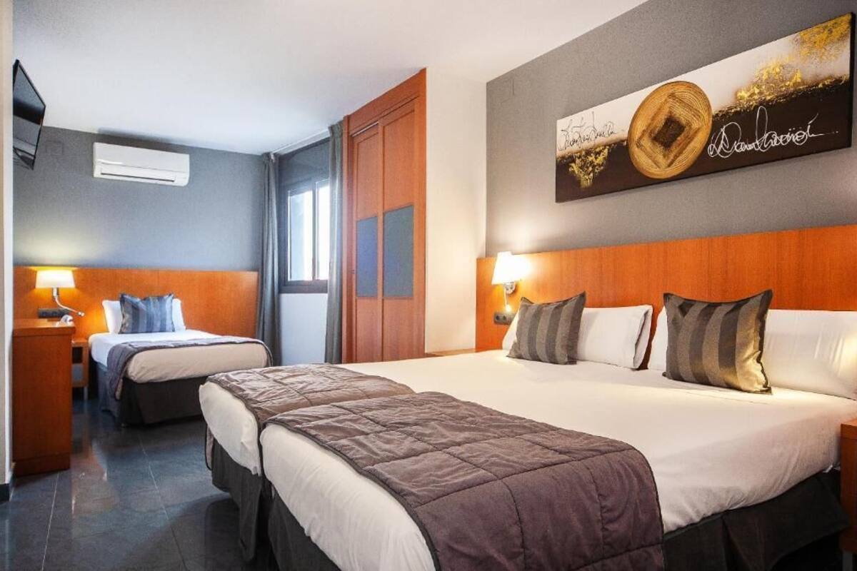 A hotel room with two beds, a wooden headboard, a wall-mounted artwork, and a bedside lamp.