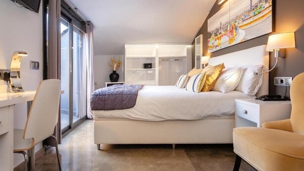 Quarto de hotel moderno com uma cama grande, uma escrivaninha e uma cadeira. Há um guarda-roupa e um quadro na parede.