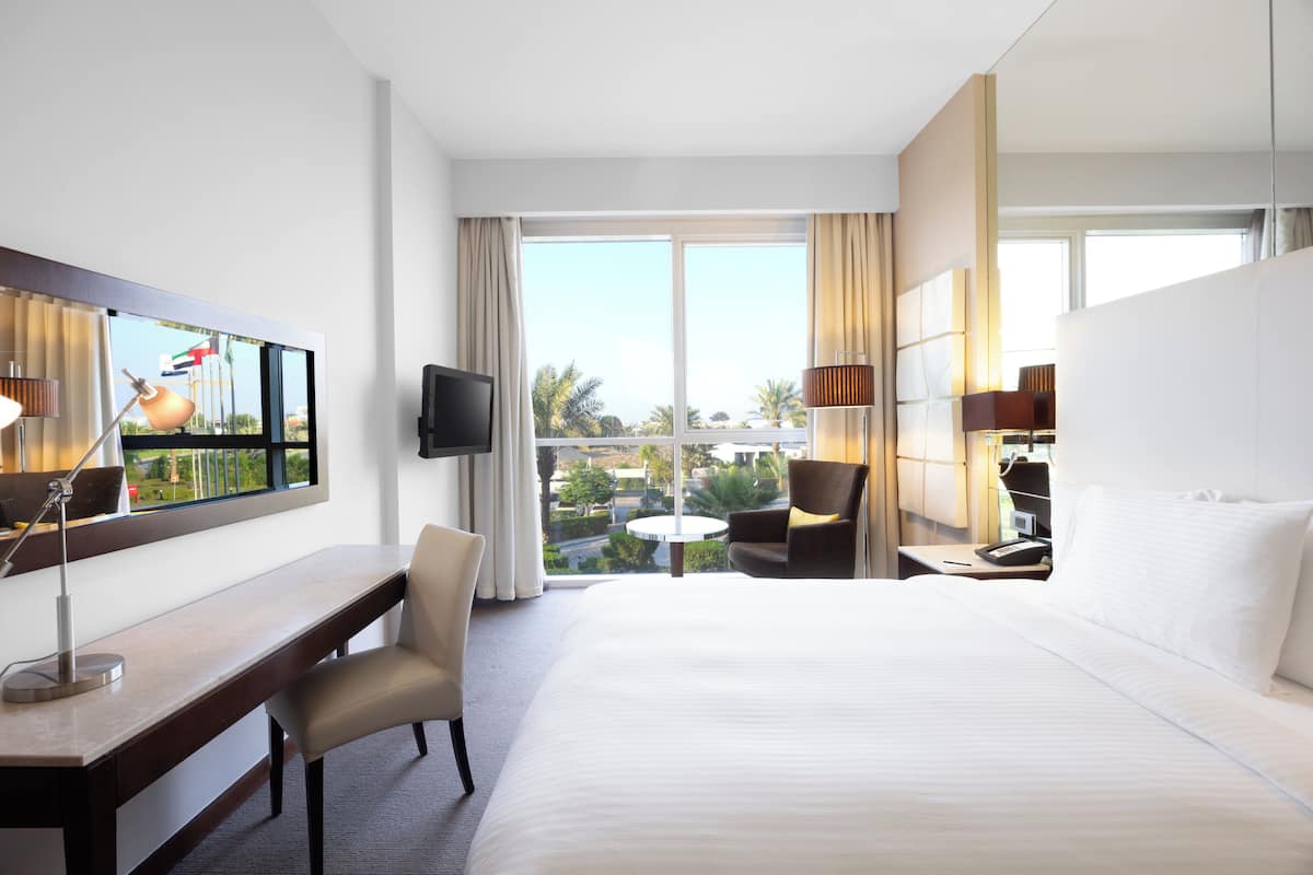 A hotel room with a large bed, a desk, a chair, a TV, and a view of the outdoors.