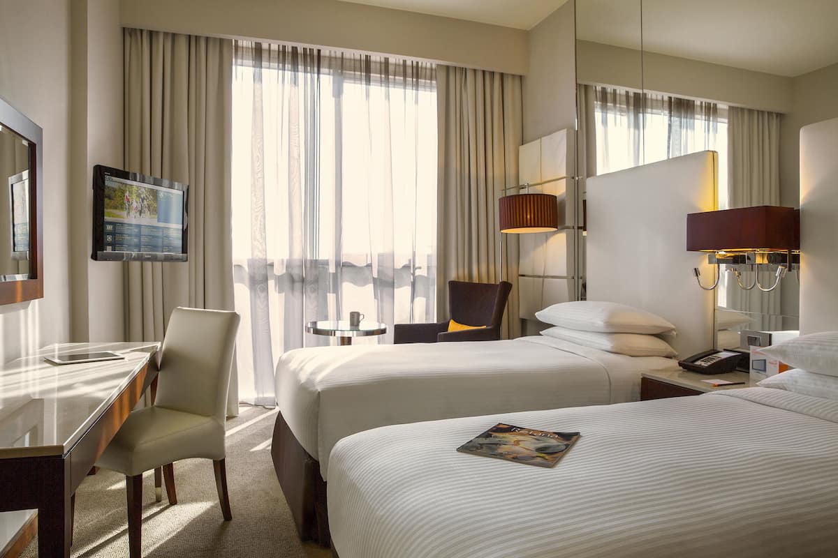A hotel room with two beds, a desk, a chair, a TV, and a window with curtains.