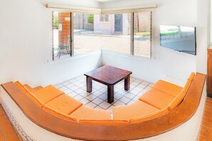 Una habitación de esquina con un sofá de madera curvada, una pequeña mesa de madera y un televisor montado en la pared.