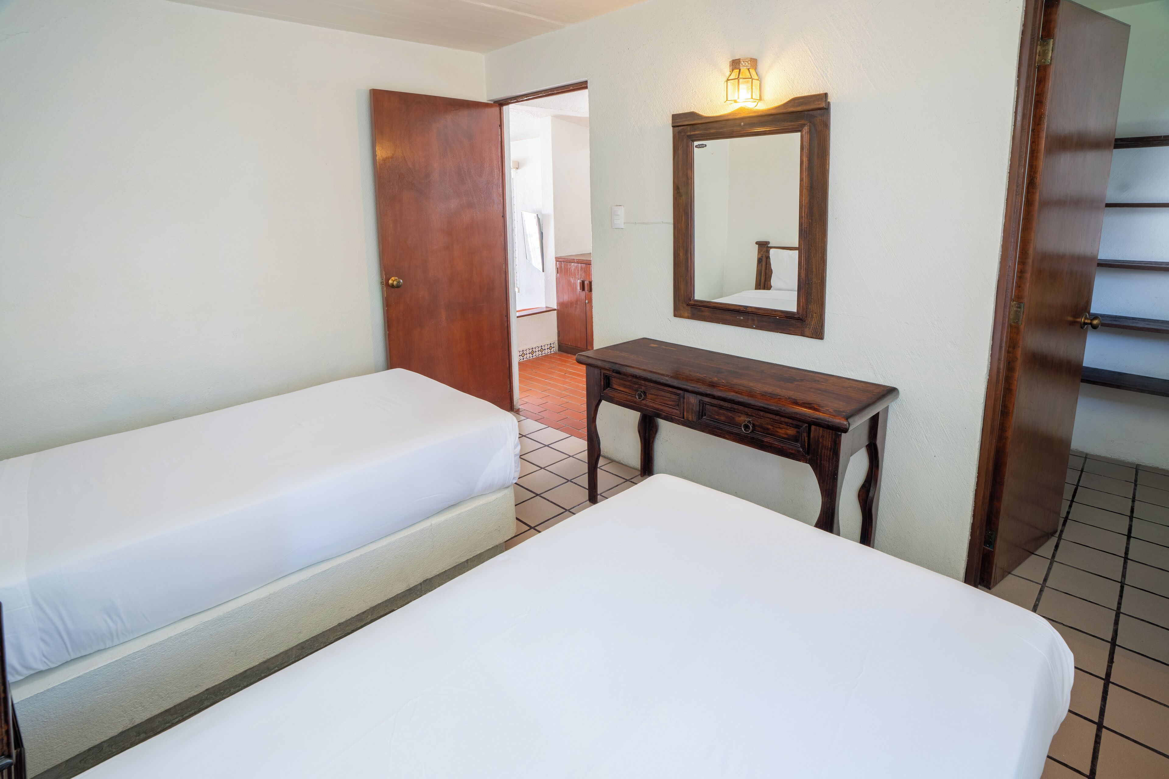 A hotel room with two single beds, a wooden dresser, and a mirror with a light fixture.