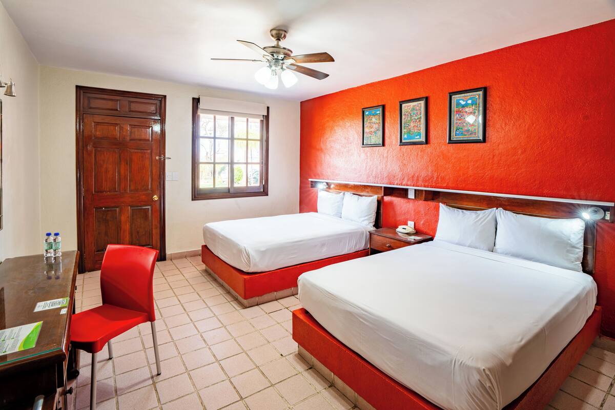 A hotel room with two beds, a desk with a chair, a window, and a ceiling fan.