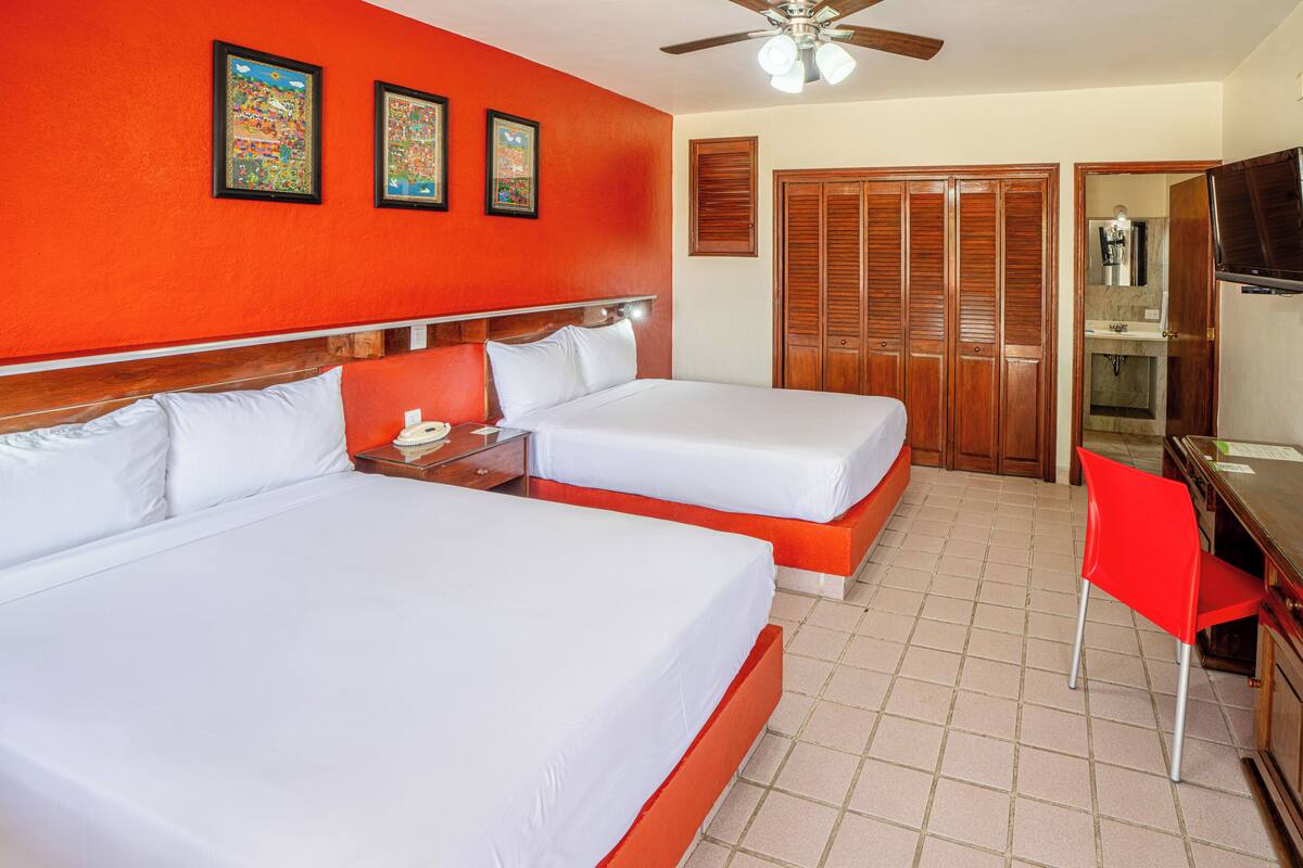 A hotel room with two beds, a desk, a chair, a television, and a wardrobe.