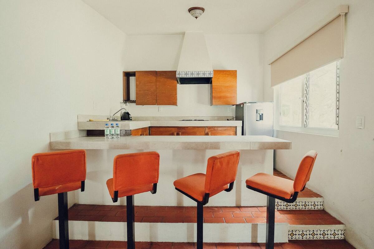 A compact kitchen with a bar area, wooden cabinets, and a window with blinds.