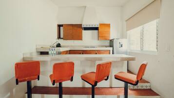 A compact kitchen with a bar area, wooden cabinets, and a window with blinds.