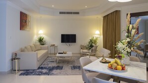 A modern living room with a sofa, coffee table, TV, and dining area with a fruit bowl. - Corp Executive Hotel Doha Suites (Doha)