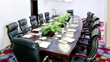 A conference room with a long table, black leather chairs, and a potted plant.