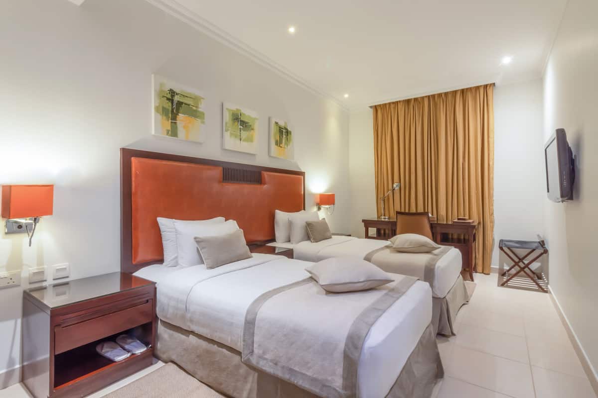 A hotel room with two beds, a wooden headboard, a flat-screen TV, and artwork on the wall.