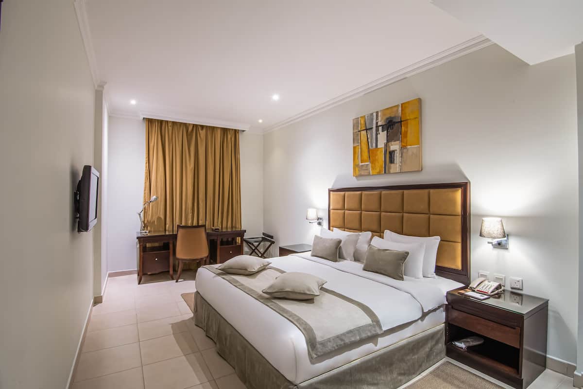 A hotel room with a large bed, bedside tables, a desk with a chair, and a television.