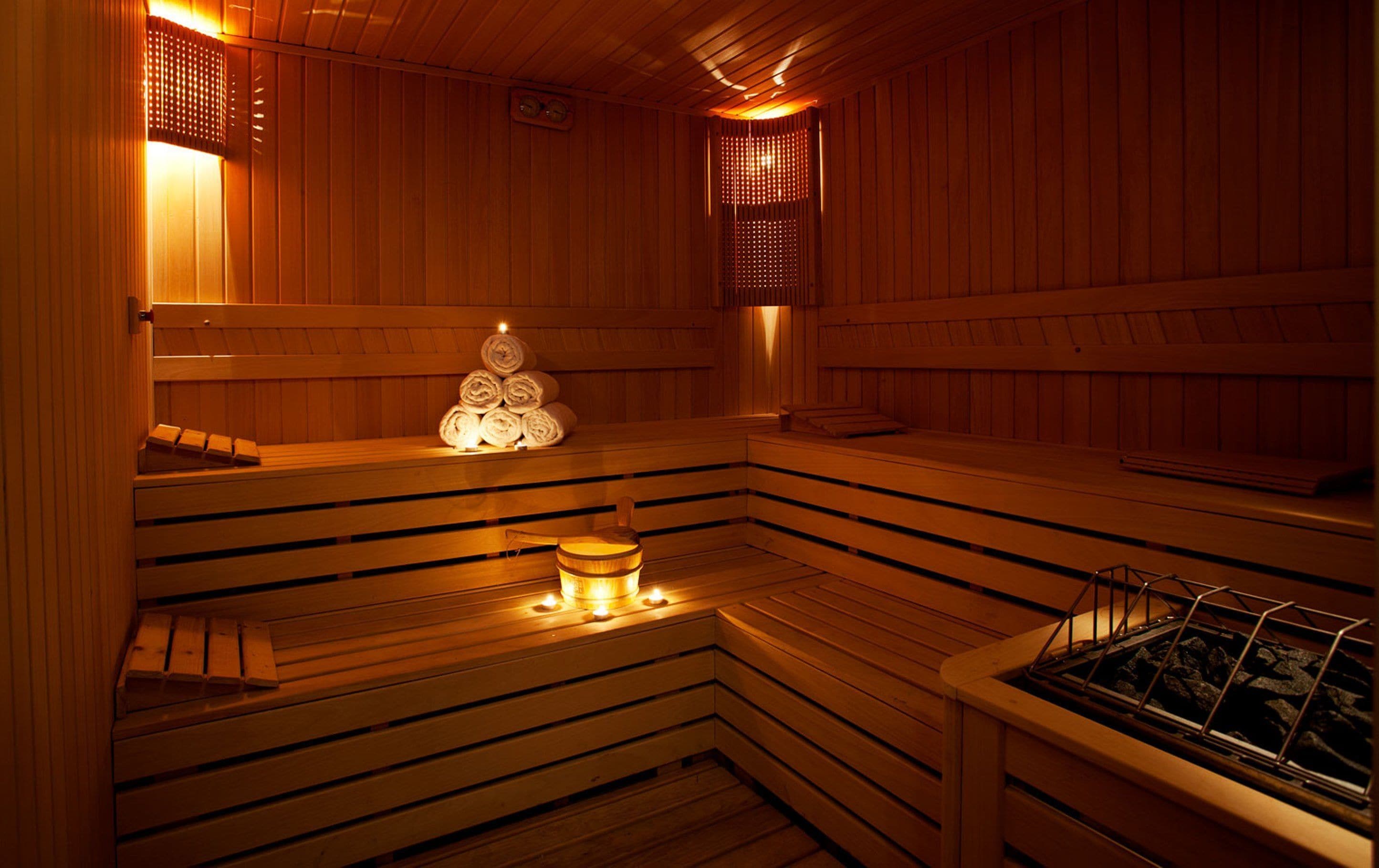 A wooden sauna with benches, a stack of towels, and a heater.