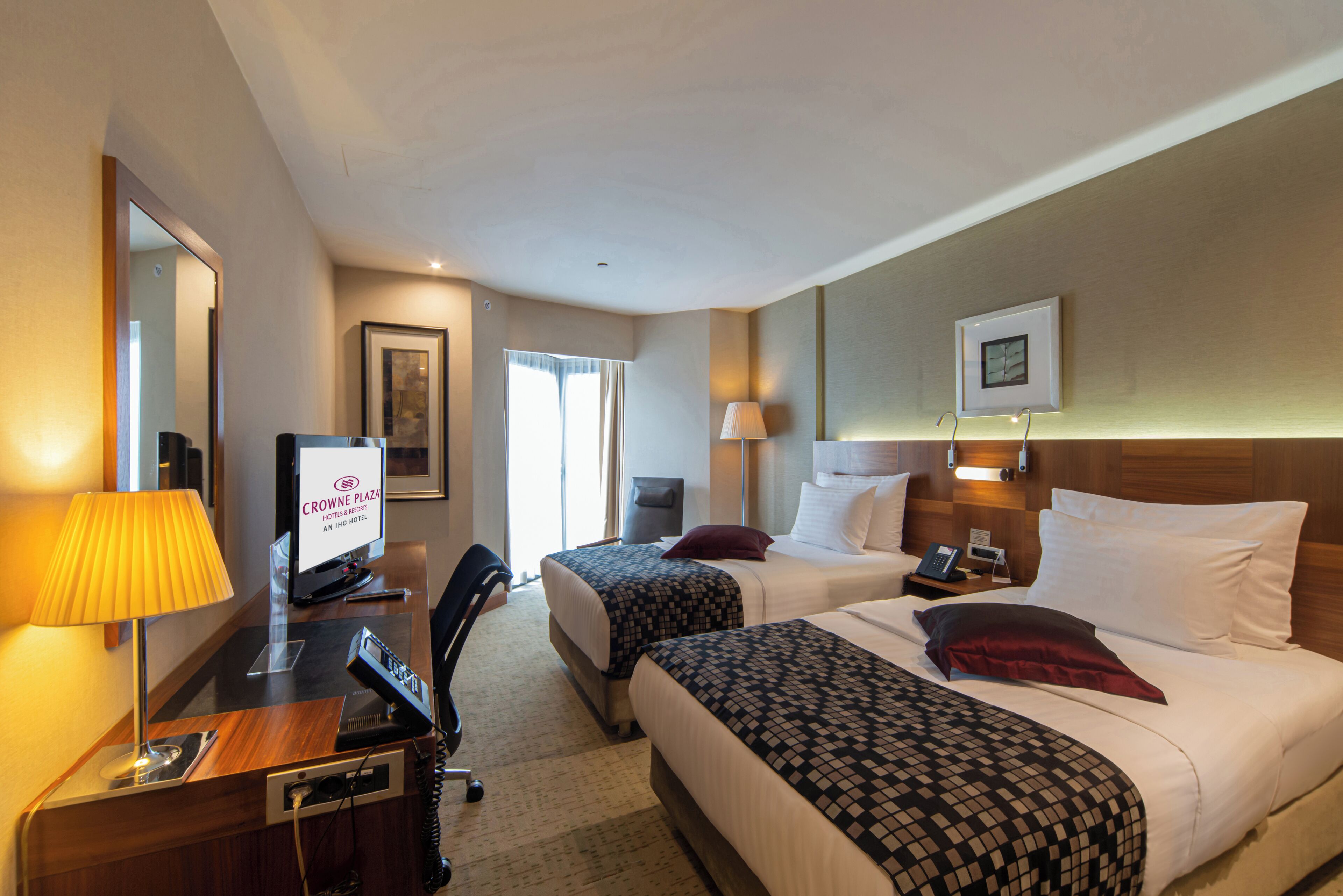 A hotel room with two beds, a desk with a telephone, a television, and a lamp.