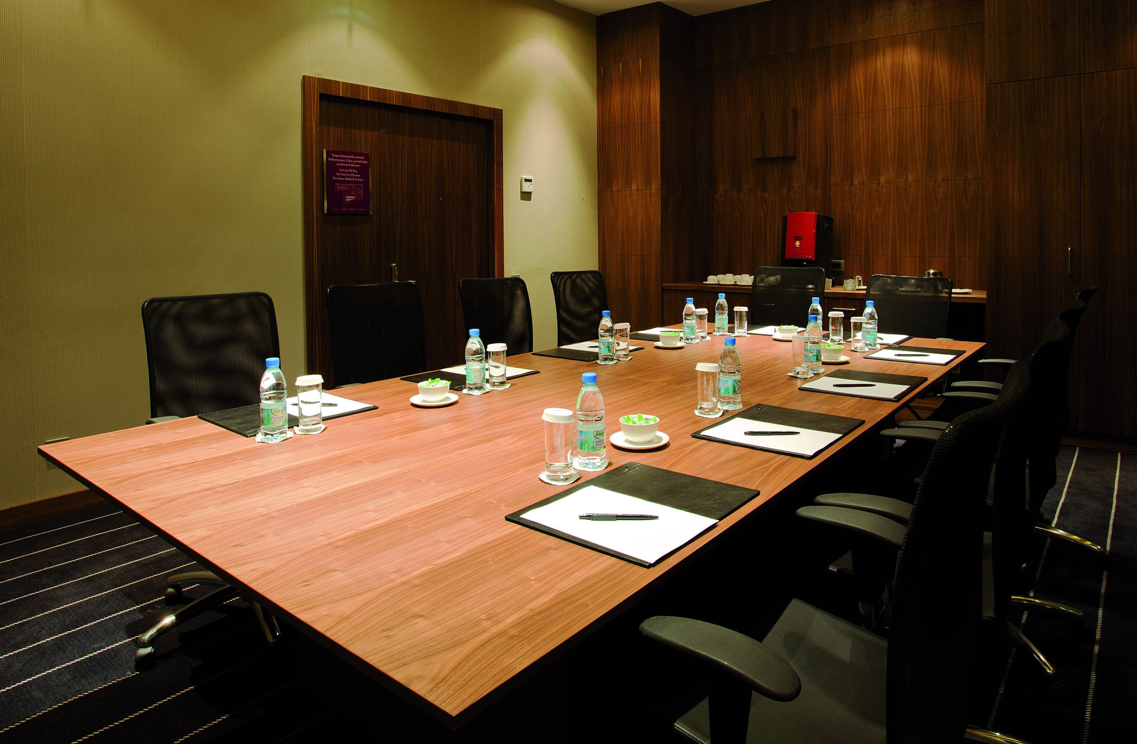 A conference room with a long wooden table, multiple chairs, water bottles, and a coffee machine.