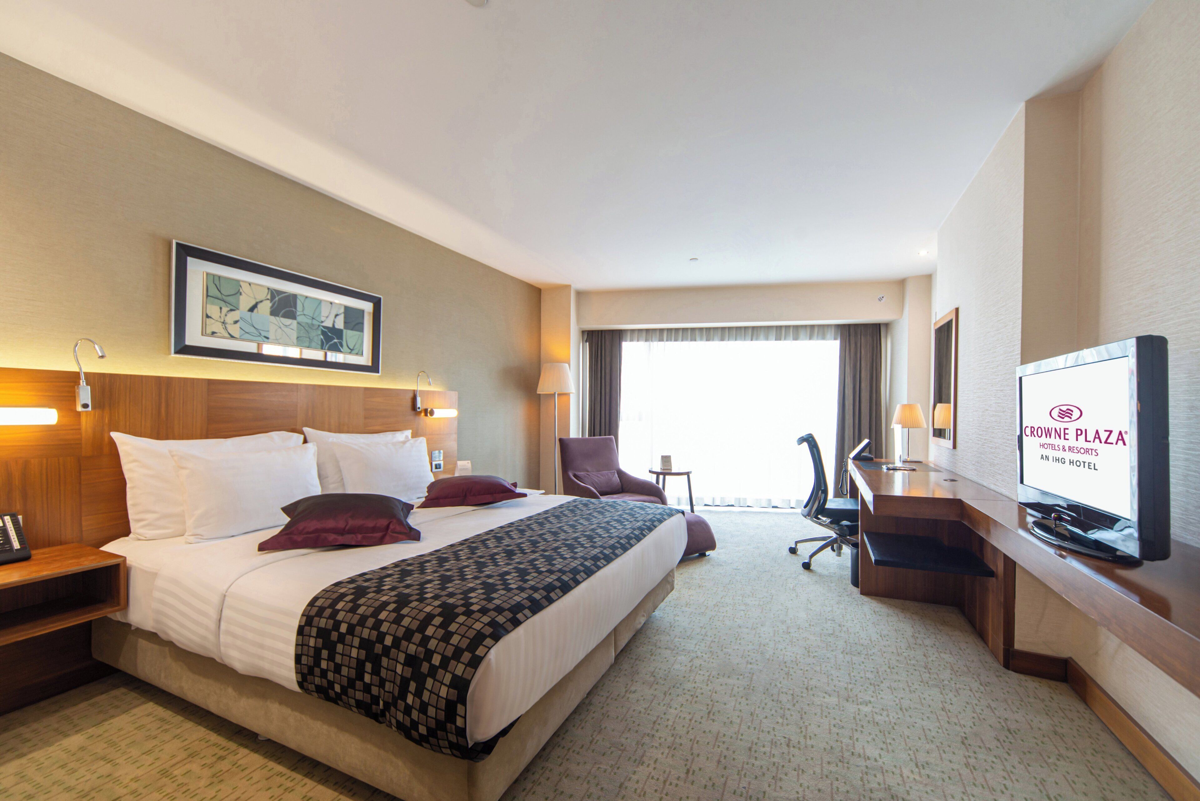 A hotel room with a bed, a desk, a chair, a television, and a window.