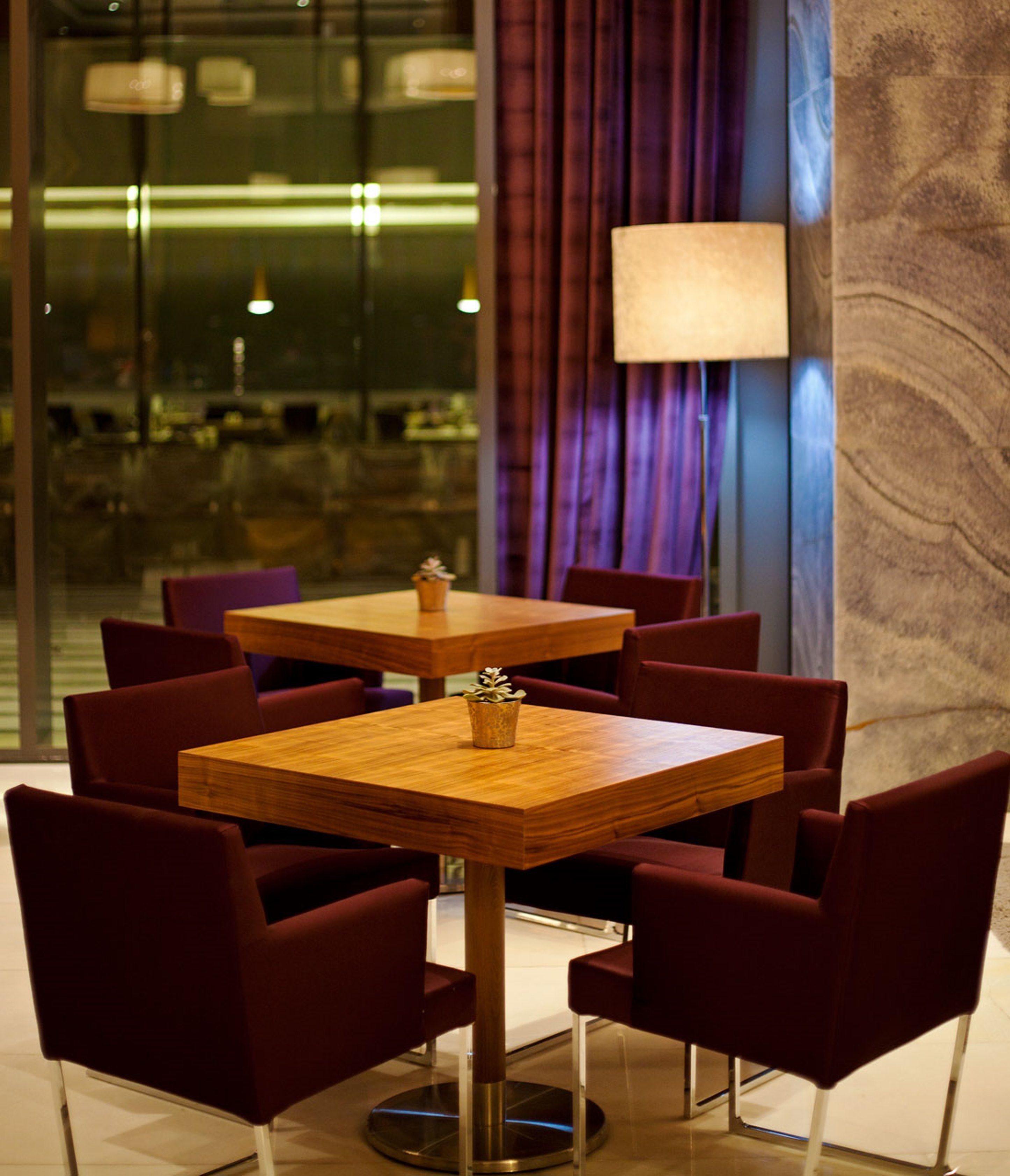 A dining area with a wooden table and six chairs, a potted plant on the table, and a large window with curtains.
