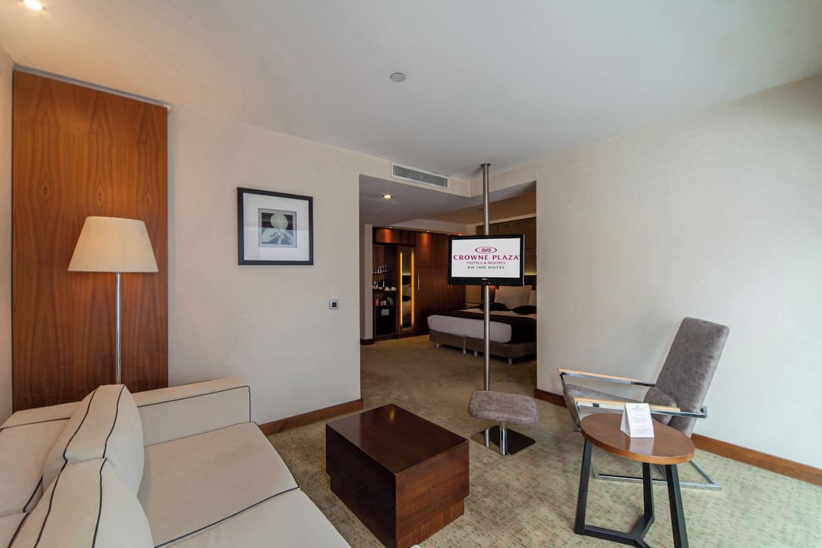 A hotel room with a sofa, a coffee table, a chair, a TV, and a sign indicating the hotel name.