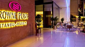A hotel entrance with a neon sign for Crowne Plaza Istanbul-Harbiye, outdoor seating area, and potted plants.