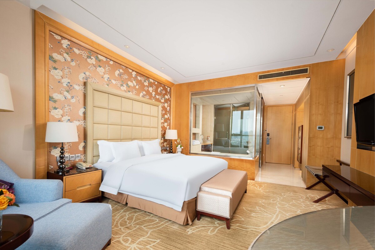 A hotel room with a large bed, a seating area, a desk, and a television.